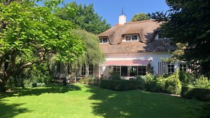 A traditional house with a thatched roof, surrounded by lush greenery and a well-maintained lawn. - 60 m2 luxury apartment with double jacuzzi and private Finnish sauna, in villa (Oss)