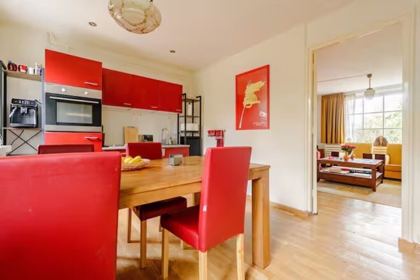 Une cuisine moderne avec des meubles rouges, un coin repas avec des chaises rouges et un salon avec un canapé et une table basse.