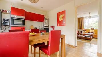 Een moderne keuken met rode kastjes, een eethoek met rode stoelen en een woonkamer met een bank en een salontafel.