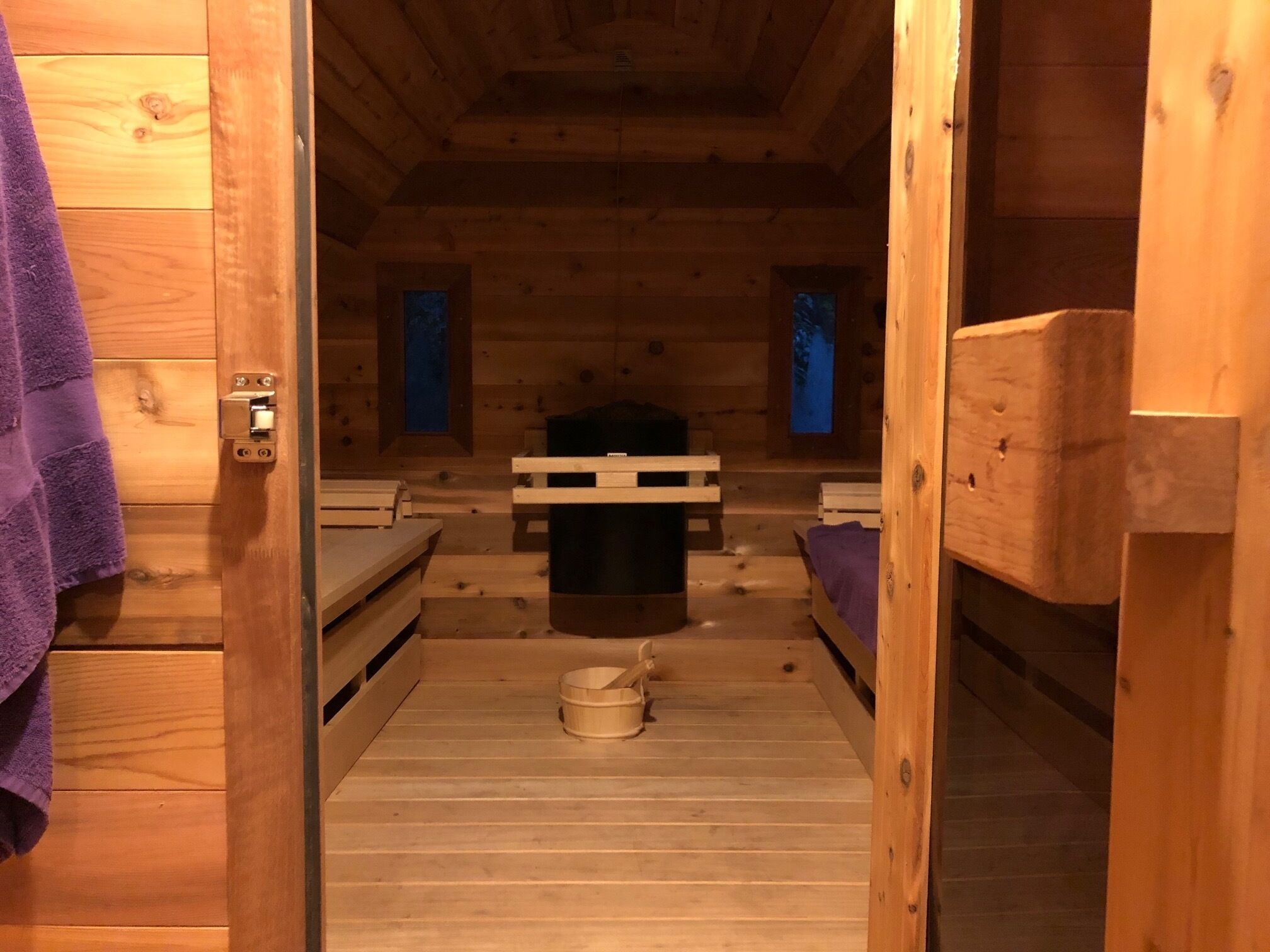 A wooden cabin with bunk beds, a central table, and a small wooden stool.