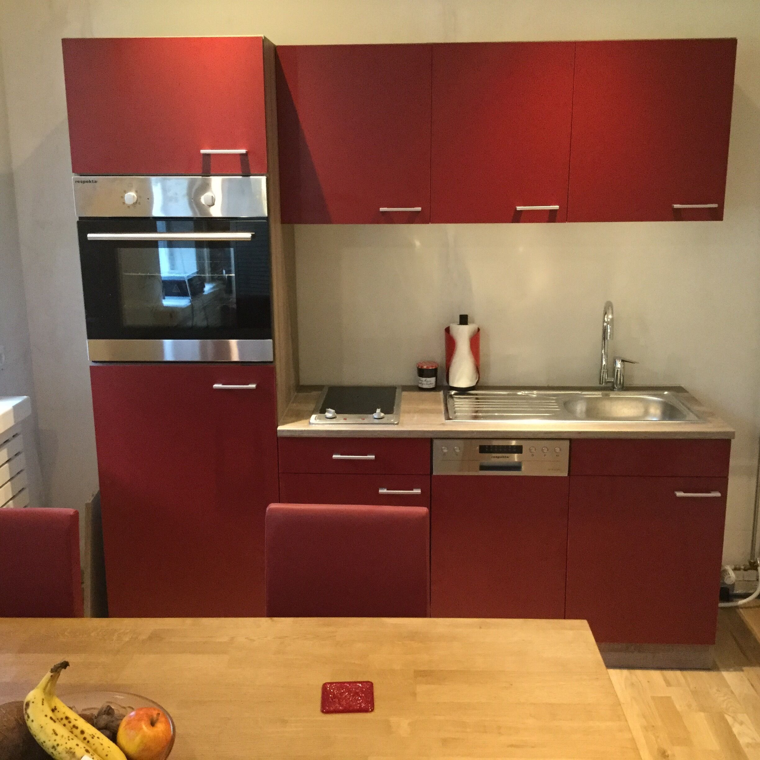 Una cuina compacta amb armaris vermells, un forn d'acer inoxidable i un rentaplats.