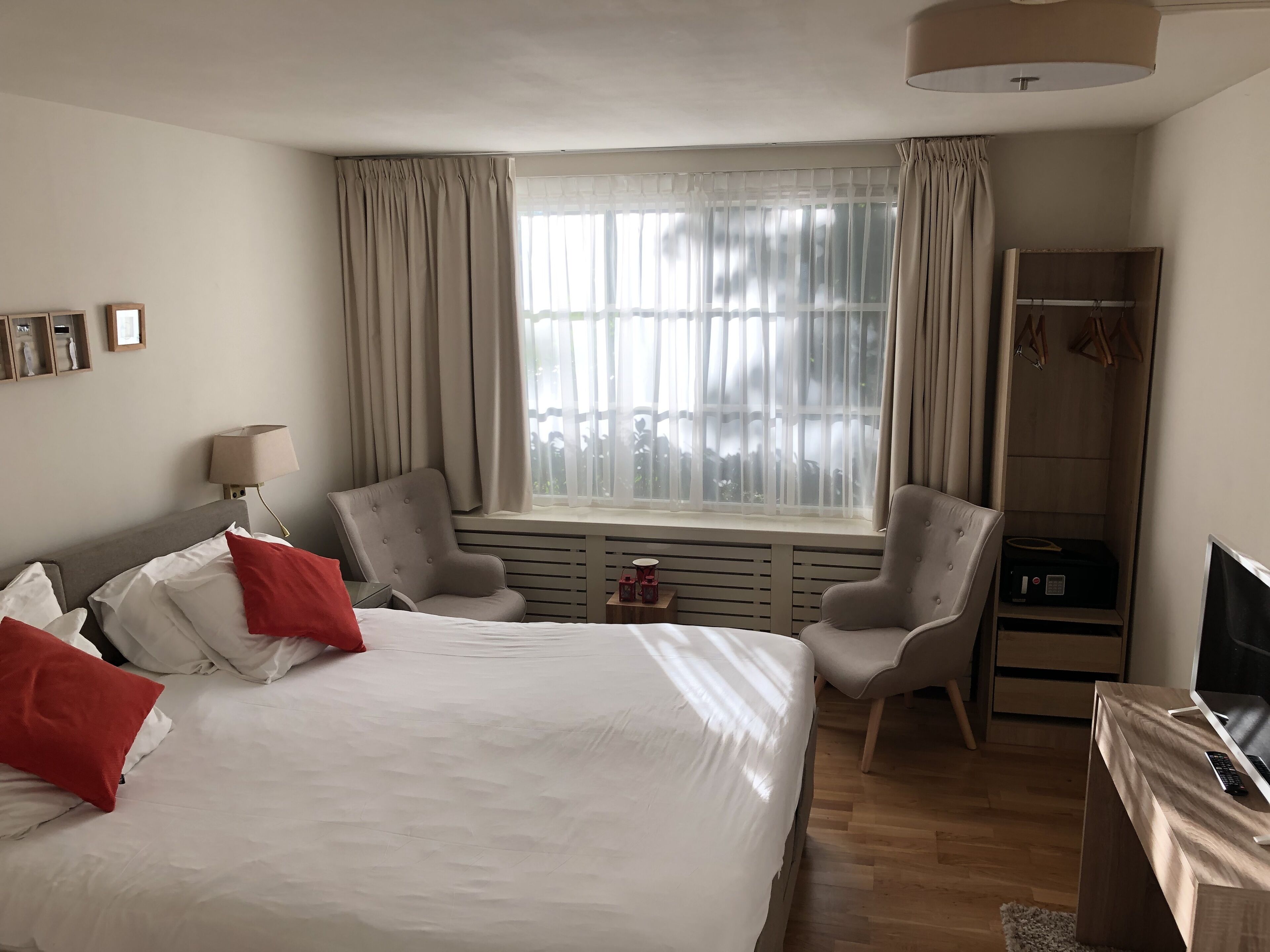 Una habitación de hotel con una cama grande, dos sillones, un televisor y un armario.