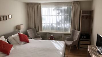 Una habitación de hotel con una cama grande, dos sillones, un televisor y un armario.