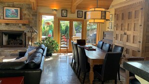 Un salon chaleureux avec une cheminée, un coin repas avec une table et des chaises en bois, et une cuisine avec des meubles en bois.