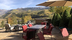 Une terrasse extérieure avec une table et des chaises, un grand parasol et une vue imprenable sur les montagnes.