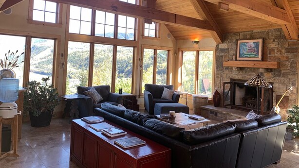 Un salon spacieux, doté d’un grand canapé d’angle, d’une cheminée et de grandes fenêtres offrant une vue sur les montagnes.
