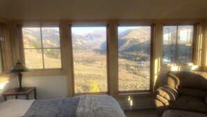 Une chambre dotée d’un grand lit, d’un fauteuil et offrant une vue sur un paysage montagneux grâce à de grandes fenêtres.