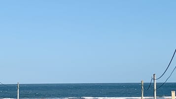 A beach with a sandy landscape, a few people, and a car parked on the left.