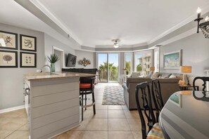 A modern kitchen with a dining area, a living room with a sofa, and a balcony with a view.