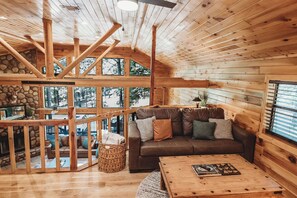 L’intérieur d’un chalet en bois, avec un plafond en bois, un mur en pierre, un canapé en cuir marron et une table basse en bois.