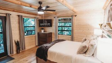 Une cabane en bois avec un lit, un ventilateur de plafond, une commode et une fenêtre donnant sur la forêt.