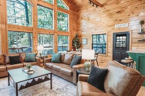 Ein Holzblockhaus-Interieur mit großem Fenster, einer Couch, einem Couchtisch und einer Küchenzeile.