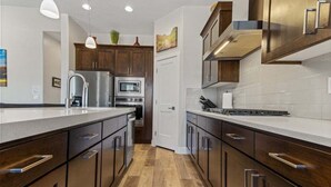 Una cucina moderna con mobili in legno scuro, elettrodomestici in acciaio inossidabile e un piano di lavoro bianco.