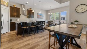 Una cucina moderna con mobili in legno, un'isola centrale con sgabelli da bar, illuminazione a sospensione e un orologio grande appeso al muro.