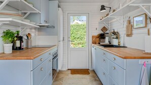 Une cuisine étroite avec des meubles de couleur bleu clair, des plans de travail en bois et une vue sur l’extérieur par la porte.