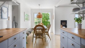 Une cuisine moderne avec des meubles blancs, un plan de travail en bois et un coin repas agrémenté de chaises en osier et d’un luminaire suspendu.