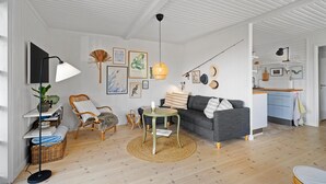 Un salon moderne avec un canapé gris, des fauteuils en osier, une table basse ronde et un lampadaire.