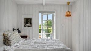 Une chambre à coucher avec un grand lit, une table de chevet, une lampe, un tableau encadré et une fenêtre donnant sur un paysage verdoyant.