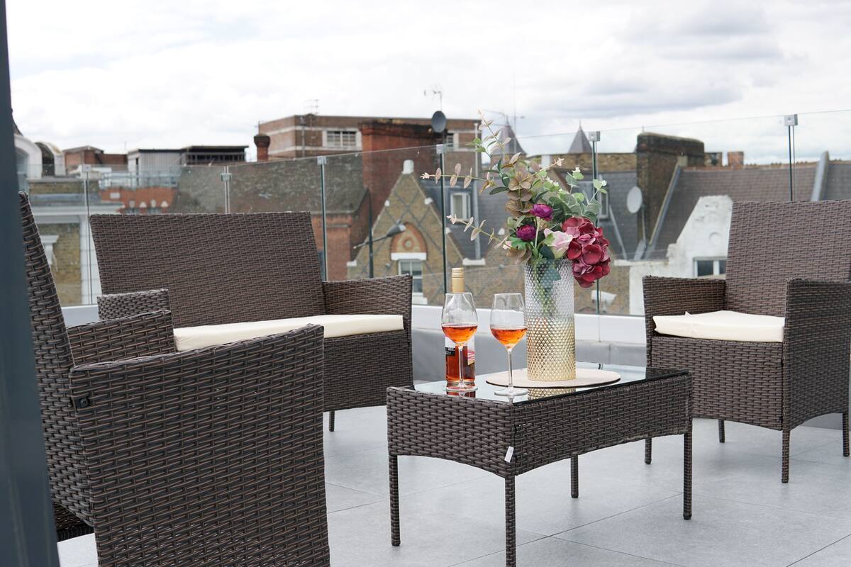 A rooftop terrace with wicker furniture, a table with drinks, and a vase with flowers.
