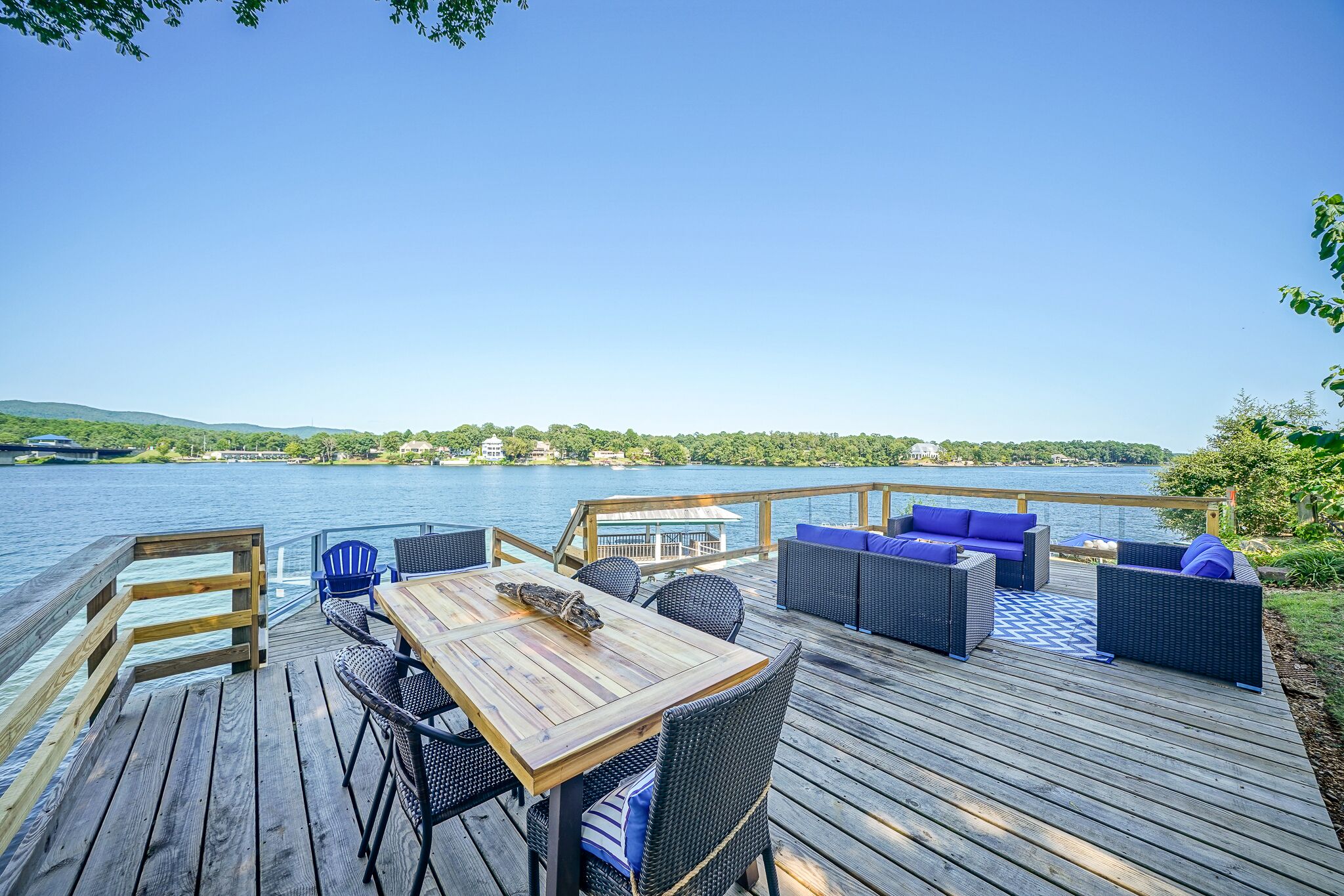 A wooden deck with outdoor furniture, a table, and a view of a lake and distant hills.