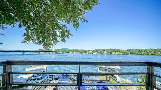 A wooden deck with a view of a river, docked boats, and a distant bridge.