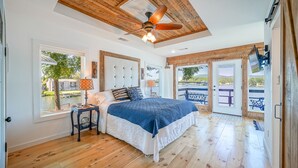 A bedroom with a large bed, wooden ceiling, and a view of a patio with outdoor seating.