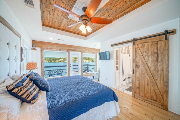 A bedroom with a large bed, a ceiling fan, a view of the outdoors, and a sliding barn-style door.