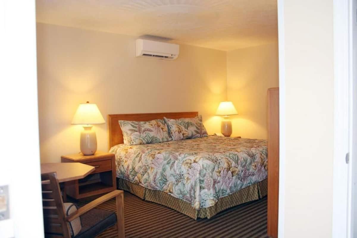 Ein Hotelzimmer mit einem Bett, zwei Nachttischlampen, einem Schreibtisch mit Stuhl und einer Klimaanlage.