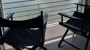 A balcony with two black chairs, overlooking a lake with a forested hillside in the background. - Lake Front Hotel (Cooperstown)