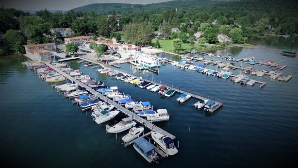 An aerial view of a marina with numerous boats docked, surrounded by residential buildings and lush greenery. - Lake Front Hotel (Cooperstown)