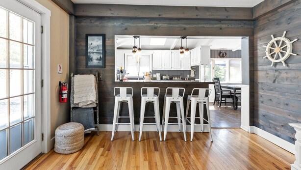 Cocina moderna con detalles de madera, una barra con taburetes blancos y vista al comedor.