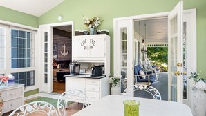 Una habitación acogedora con una mesa de comedor, una zona de cocina con armarios que dicen 'COFEE SHOP' y vistas del patio exterior con mobiliario.