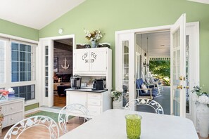 A cozy room with a dining table, a kitchen area with cabinets labeled 'COFEE SHOP', and a view of the outside patio with seating.