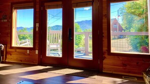 A wooden cabin with large windows, a wooden deck, and a view of mountains.