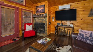 A cozy cabin interior with a stone fireplace, a television, and a red chair.