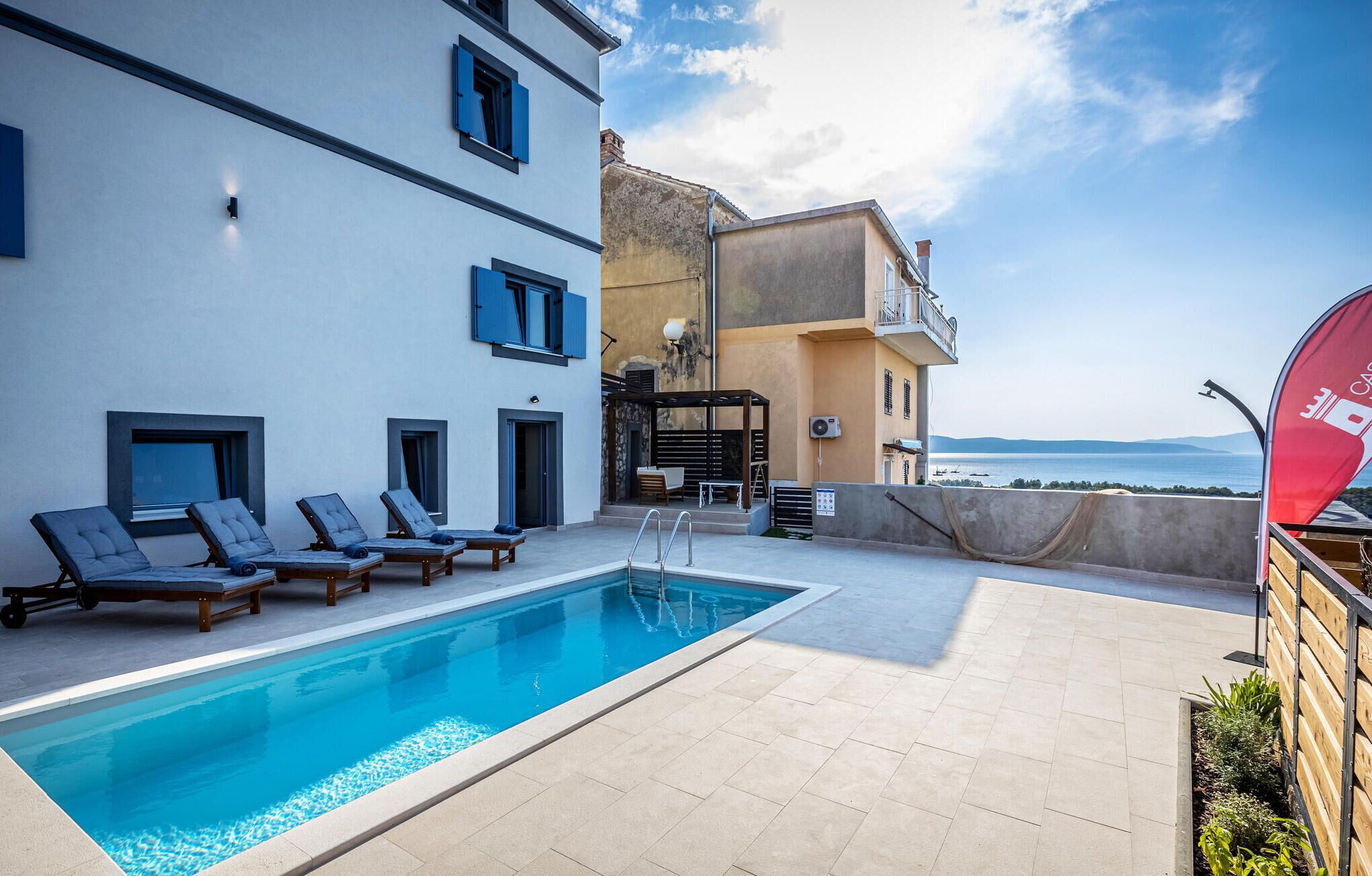 A rooftop pool area with lounge chairs and a view of the sea.