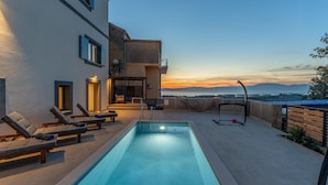 Piscina no terraço com espreguiçadeiras, área com rede e vista para o mar ao pôr do sol.