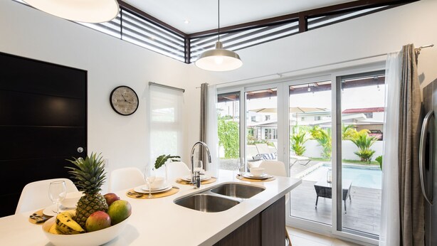 A modern kitchen with a large island, a sink, and a dining area. There is a view of a pool and outdoor seating. - Modern Stylist 3 BR Beach House, w/Private Pool & Fast WiFi. (Jaco)