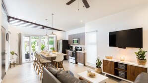 A modern kitchen with a flat-screen TV, a dining area with a long table and chairs, and a living room with a sofa and a coffee table. - Modern Stylist 3 BR Beach House, w/Private Pool & Fast WiFi. (Jaco)