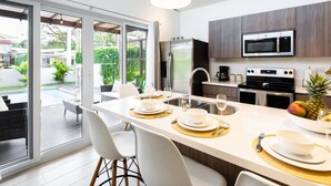 A modern kitchen with a large island, stainless steel appliances, and a view of a backyard patio. - Modern Stylist 3 BR Beach House, w/Private Pool & Fast WiFi. (Jaco)