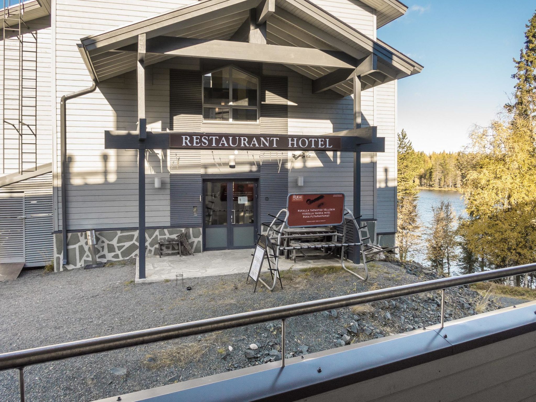 A restaurant hotel with a signboard, outdoor seating, and a view of a lake.