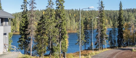 Une propriété située au bord d’un lac, avec une allée en gravier, une terrasse en bois et une vue sur le lac, entouré d’arbres.