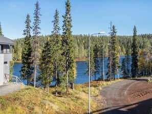 A lakeside property with a gravel driveway, a wooden deck, and a view of a lake surrounded by trees.