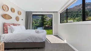 Een moderne slaapkamer met een groot bed, uitzicht op een weelderige tuin en een berg op de achtergrond.