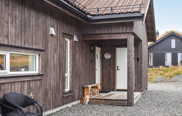 A wooden house with a front porch, a door with a circular sign, and a bench outside.