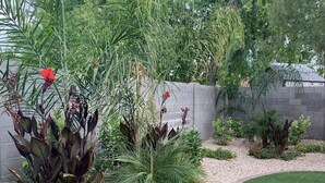 Un jardin aménagé avec une variété de plantes, un chemin sinueux en briques et une partie recouverte de gazon synthétique.