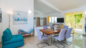 Uma sala de estar moderna com uma mesa de jantar de madeira, cadeiras azul claro, um sofá verde água e uma rede colorida.