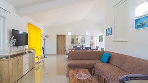 Uma sala de estar ampla, com um sofá marrom grande, uma mesa de centro de madeira e uma TV sobre um armário de madeira.