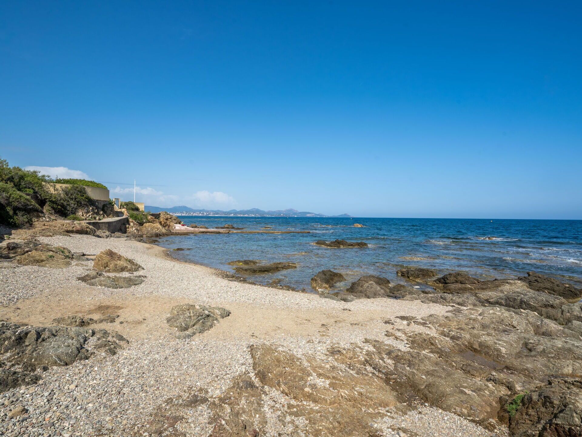 Ein felsiger Strand mit klarem, blauem Wasser und Bergen in der Ferne.