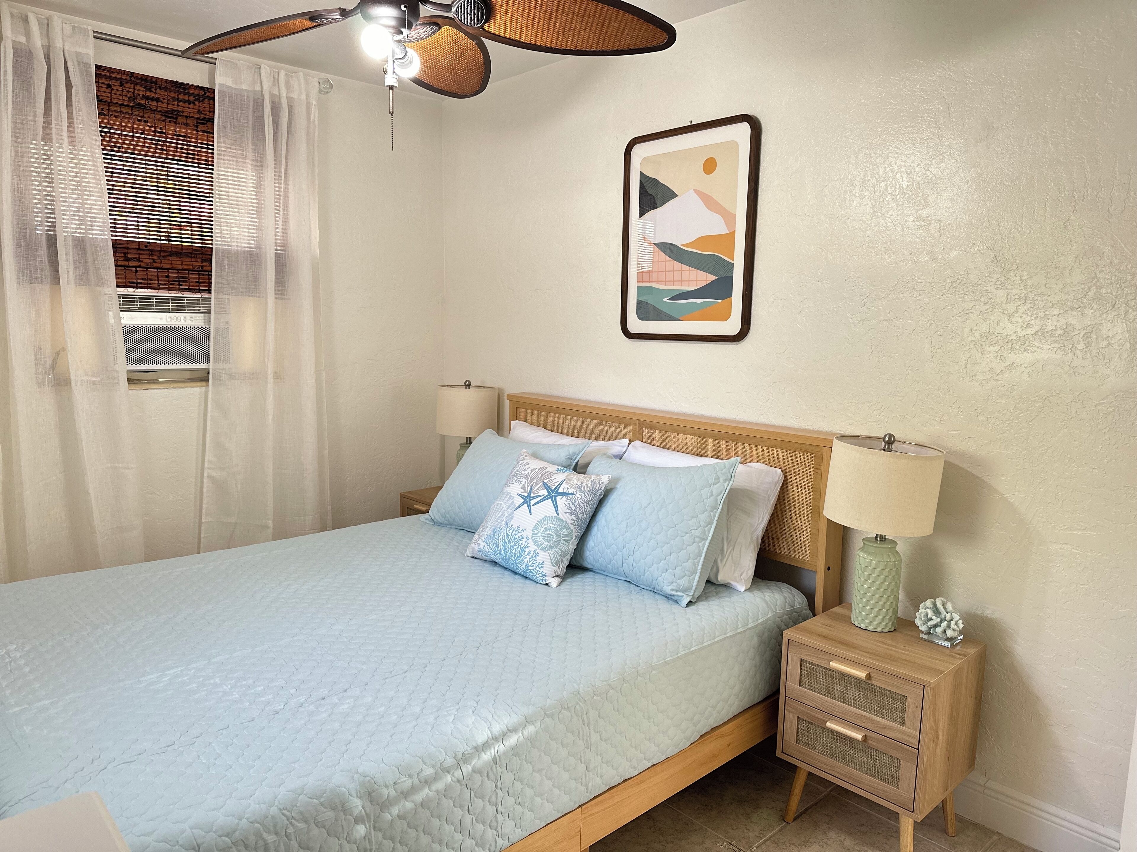 Una camera da letto ordinata con un letto, lampade da comodino, un piccolo comodino e una ventola a soffitto.